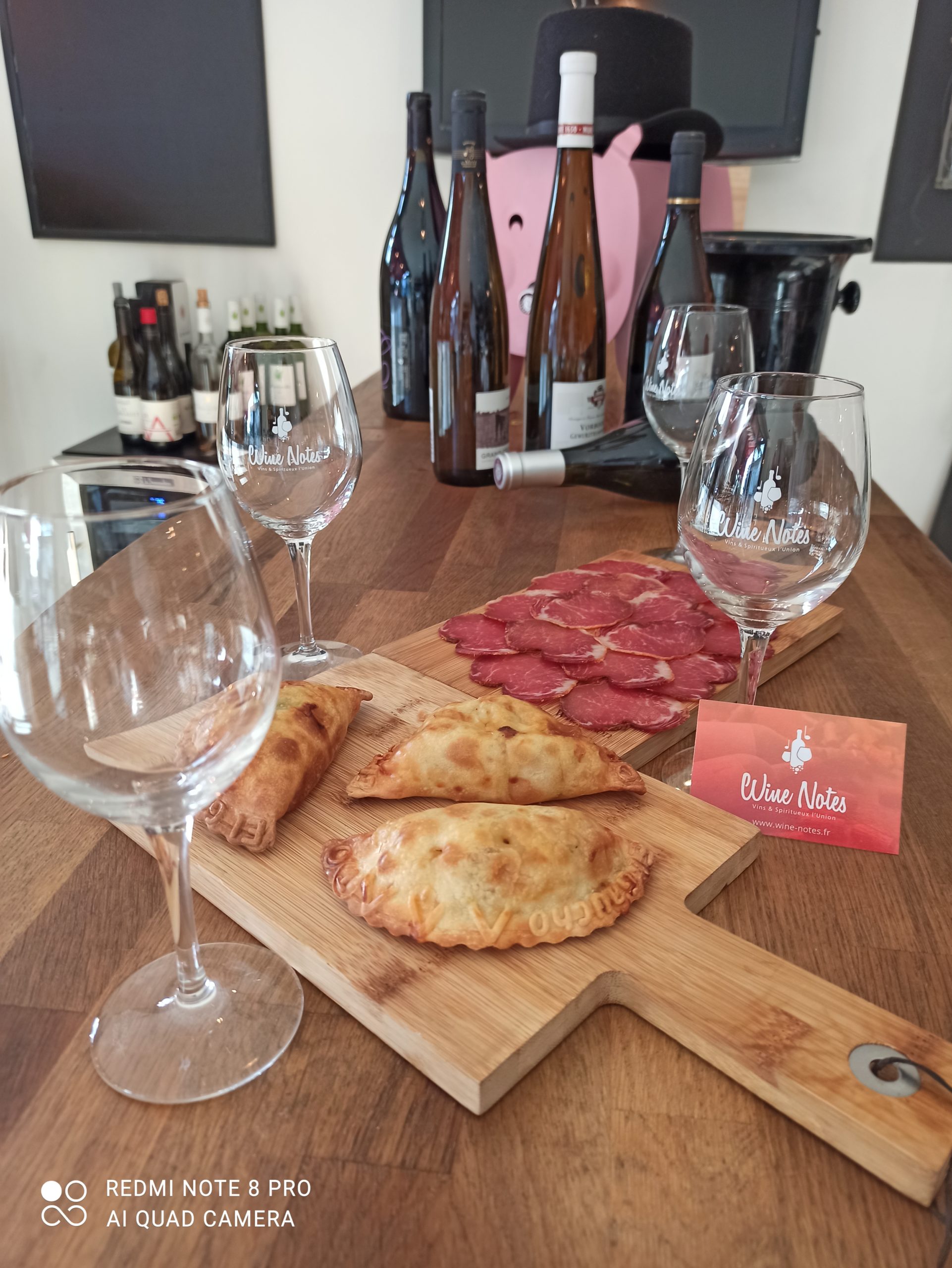 Planche de charcuteries, bouteilles de vins et empanadas disposés sur un table chez le caviste